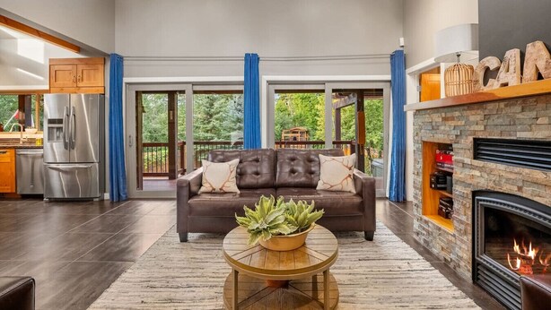 A spacious living room with a fireplace, a leather sofa, and a large window overlooking a deck.