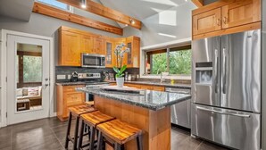 A modern kitchen with wooden cabinets, a stainless steel refrigerator, and a large island with bar stools.