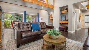 A spacious living room with a brown leather sofa, a round wooden coffee table, and a large window overlooking a garden.