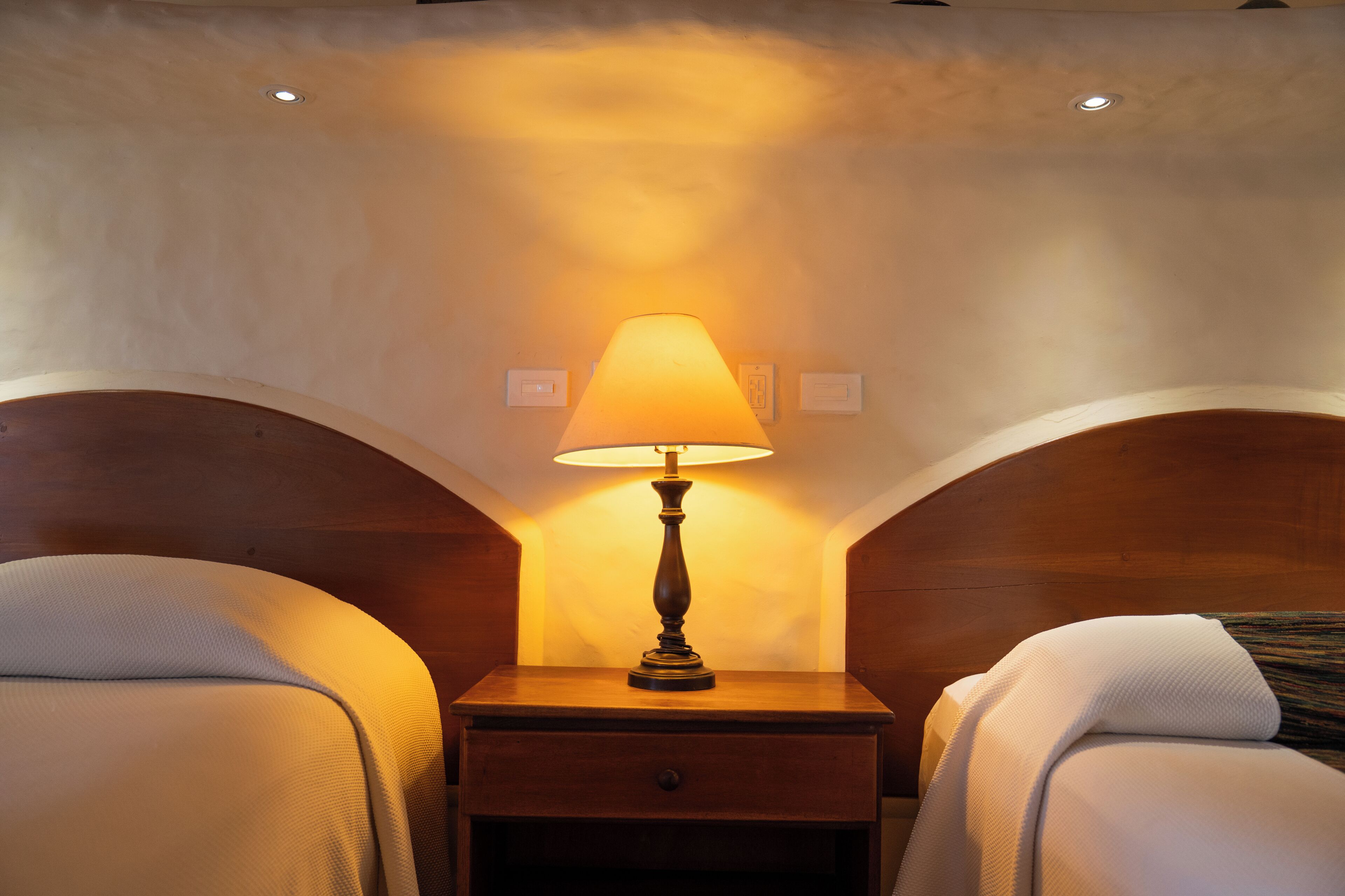 A hotel room with two beds, a nightstand with a lamp, and a small drawer.