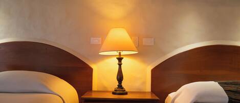 A hotel room with two beds, a nightstand with a lamp, and a small drawer.