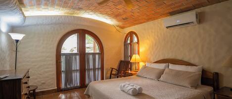 Una habitación de hotel con cama, ventilador de techo, aire acondicionado, lámpara y vista por una puerta.