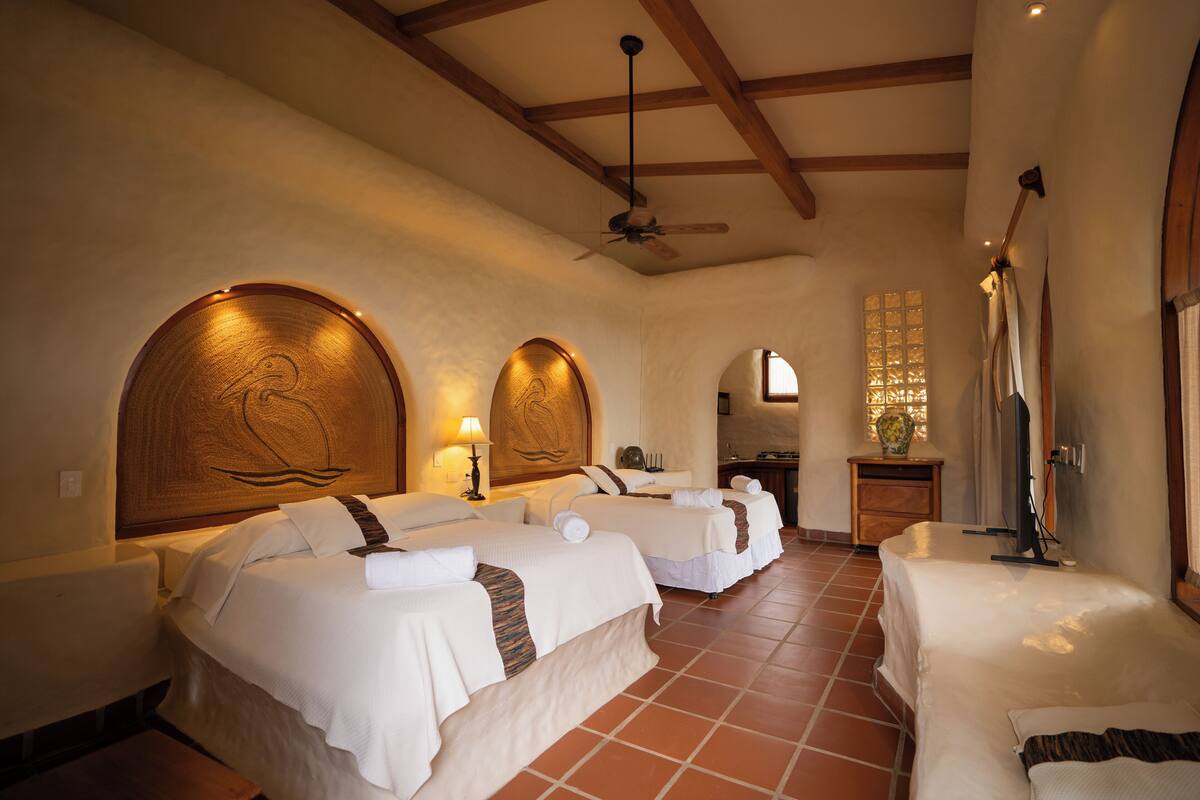 A hotel room with three beds, a ceiling fan, a TV, and a window with a view.
