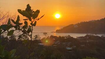 A sunset over a coastal town with visible buildings and vegetation.
