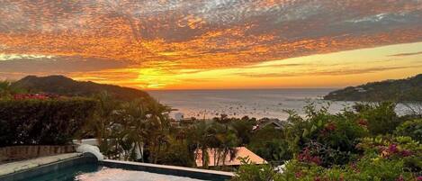 Una piscina con vistas al océano y colinas al atardecer.