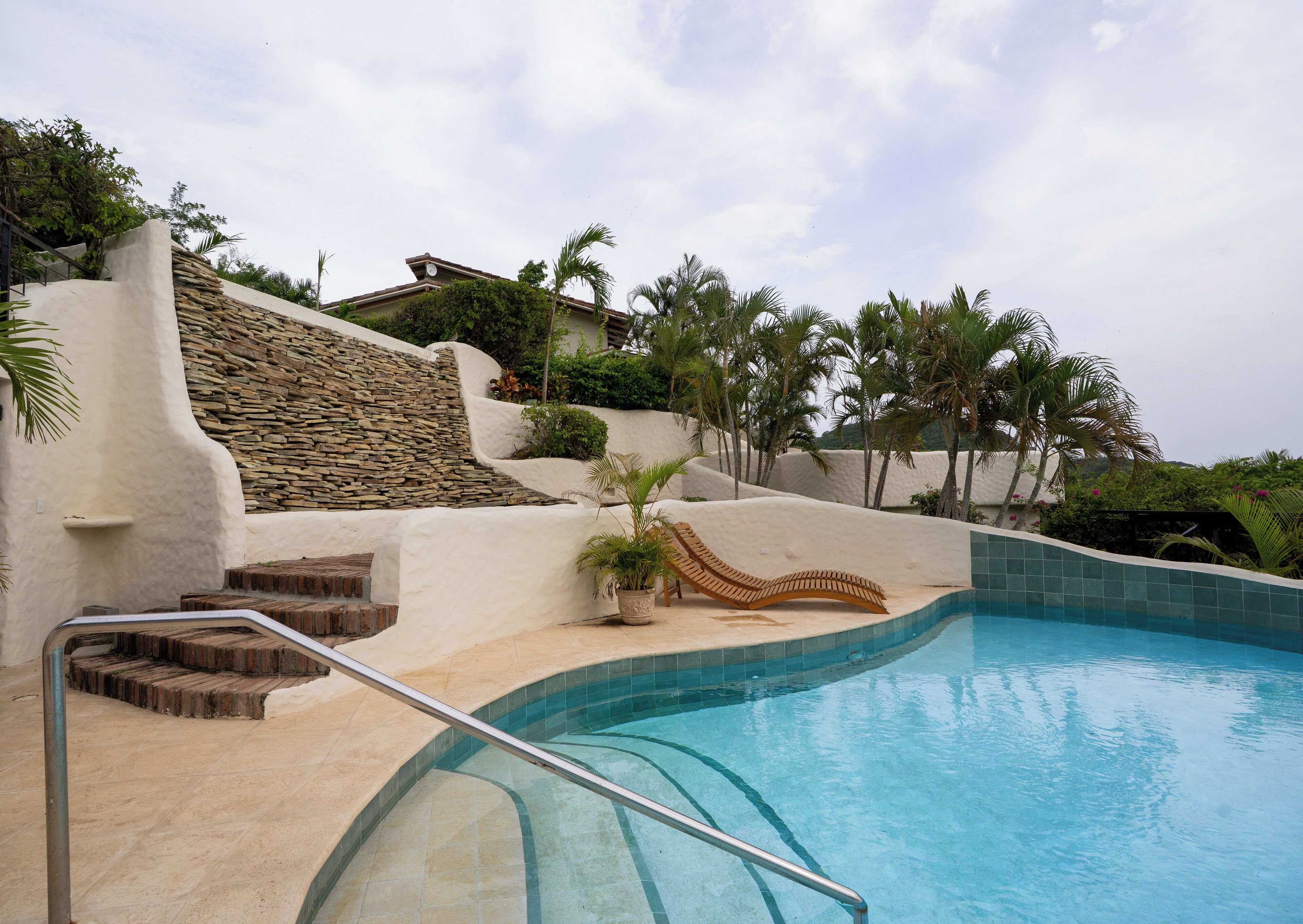 Un área de piscina con un muro de piedra, una silla de descanso y una palmera.