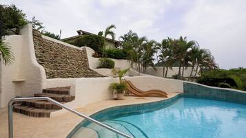 Un área de piscina con un muro de piedra, una silla de descanso y una palmera.