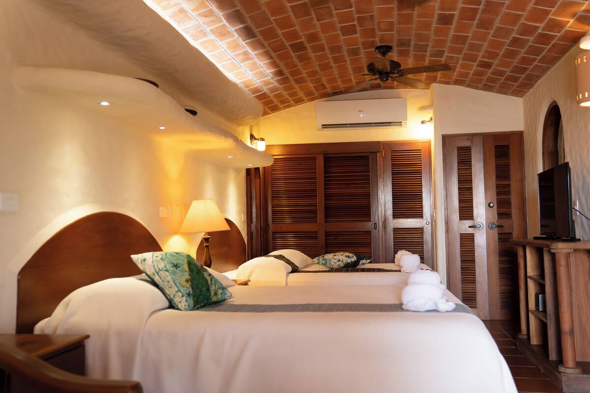 A hotel room with two beds, a ceiling fan, a TV, and a wooden door.