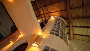 Una habitación con techo de paja, vigas de madera y varios ventanales.