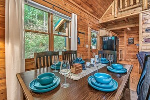 A wooden interior with a dining table set for four, a refrigerator, and a view of the outdoors.