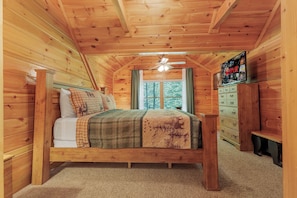Une chambre dans une cabane en bois, avec un lit, une commode, un ventilateur de plafond et une fenêtre.