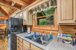 Eine Küche mit Holzausstattung, einer Edelstahlspüle und einem Fenster mit Blick auf Grünflächen.