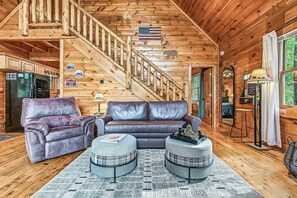 Ein Interieur einer Holzhütte mit einer Holztreppe, Ledermöbeln und Blick ins Freie.