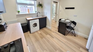 Une cuisine compacte équipée d’un lave-linge, d’un évier et d’un coin repas avec des chaises.