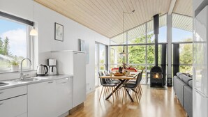 Eine moderne Küche mit weißen Schränken, ein Essbereich mit Holztisch und -stühlen sowie ein großes Fenster mit Blick auf Grünflächen.