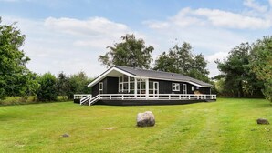 Eine schwarz-weiß gestrichene Holzhütte mit Veranda, umgeben von einer grünen Wiese und Bäumen.