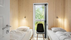 Ein Zimmer mit Holzwänden, einem großen Fenster, zwei Betten, einem Sessel und einer Tür.