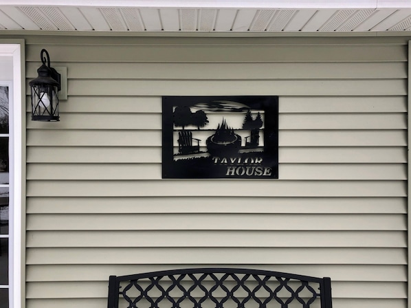 A house sign with a silhouette of a house, trees, and a bench.
