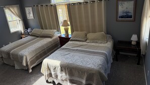 A bedroom with two beds, a window with curtains, a fan, and a lamp on a nightstand. - Relax in Waupaca and the Chain O Lakes. (Waupaca)