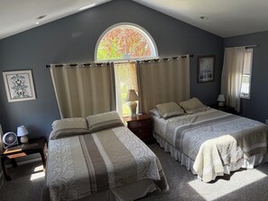 A bedroom with two beds, a large window with curtains, a fan, and a small table. - Relax in Waupaca and the Chain O Lakes. (Waupaca)