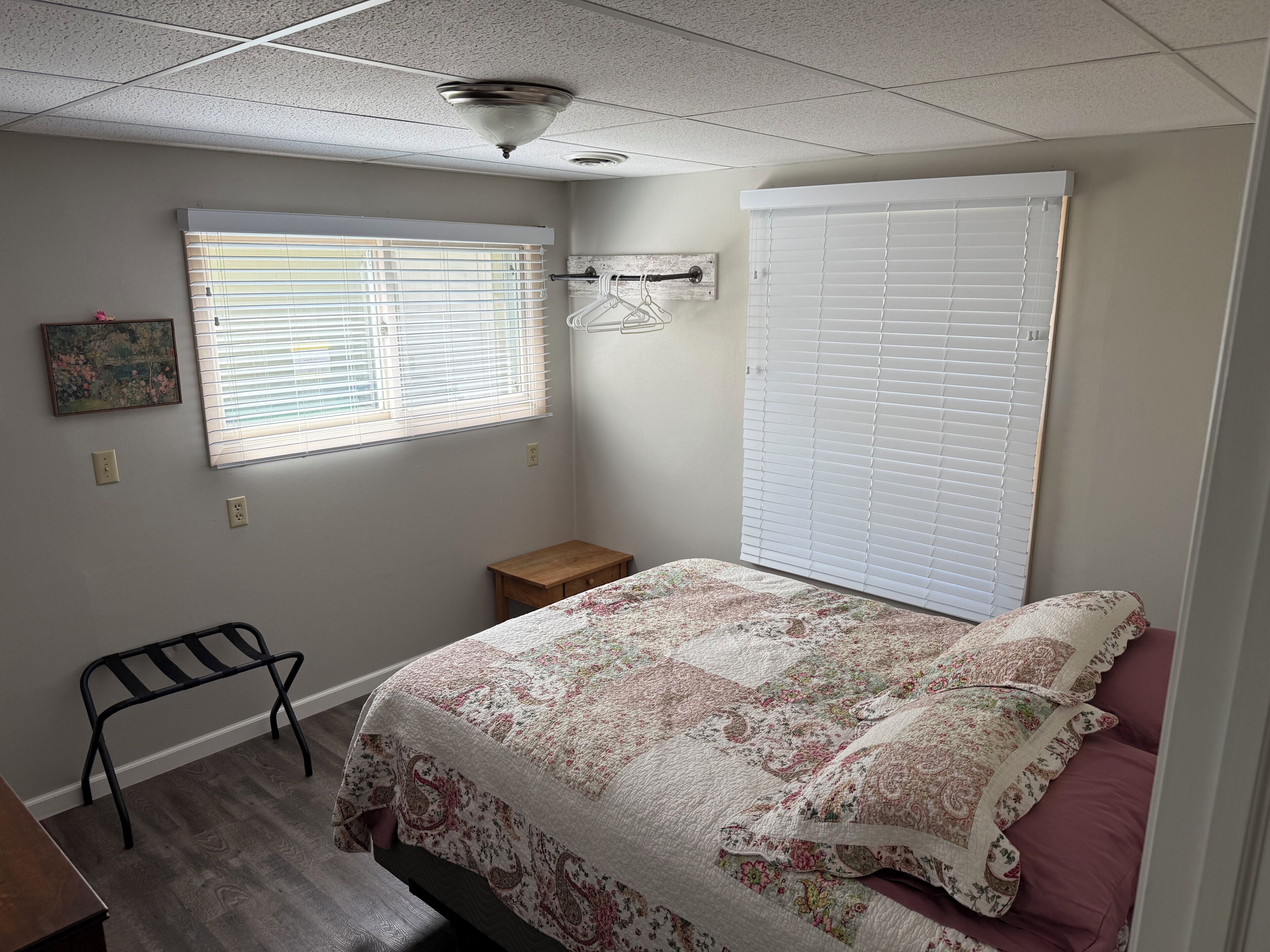 Une chambre à coucher comprenant un lit, une table de chevet, une chaise, une fenêtre avec des stores et un ventilateur de plafond.