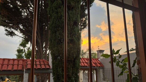 A gated area with a view of a sunset, trees, and a building with a red roof. - Pet Friendly Luxury Depa in Bugambilias (Zapopan)
