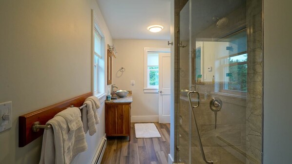 A modern bathroom with a glass shower enclosure, a wooden vanity, and a towel rack.