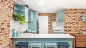 Una cocina con pared de ladrillo, armarios blancos y encimera blanca.