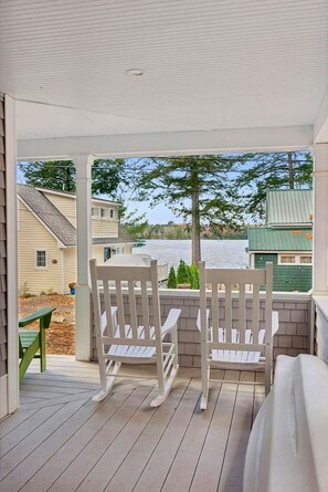 Une véranda couverte avec deux fauteuils Adirondack donnant sur un plan d’eau.