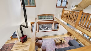 Un intérieur à plusieurs niveaux, avec des éléments en bois, comprenant une mezzanine, une cheminée et un coin salon agrémenté d’un tapis et d’une table basse en bois.