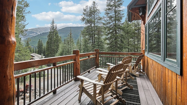 Une terrasse en bois, agrémentée de fauteuils Adirondack, qui offre une vue sur un paysage montagneux.