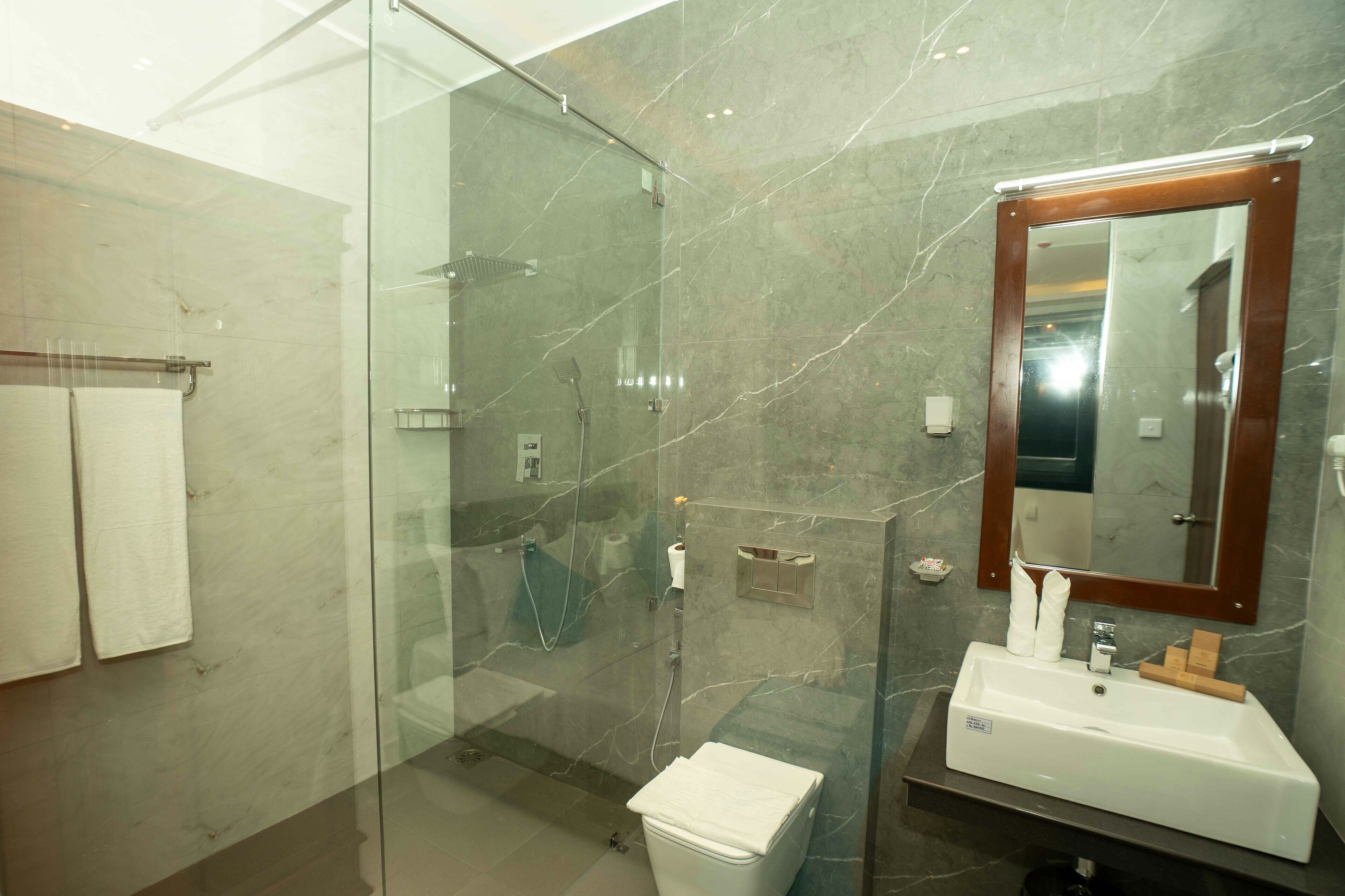 A modern bathroom with a glass-enclosed shower, a white sink, and a marble-tiled wall.