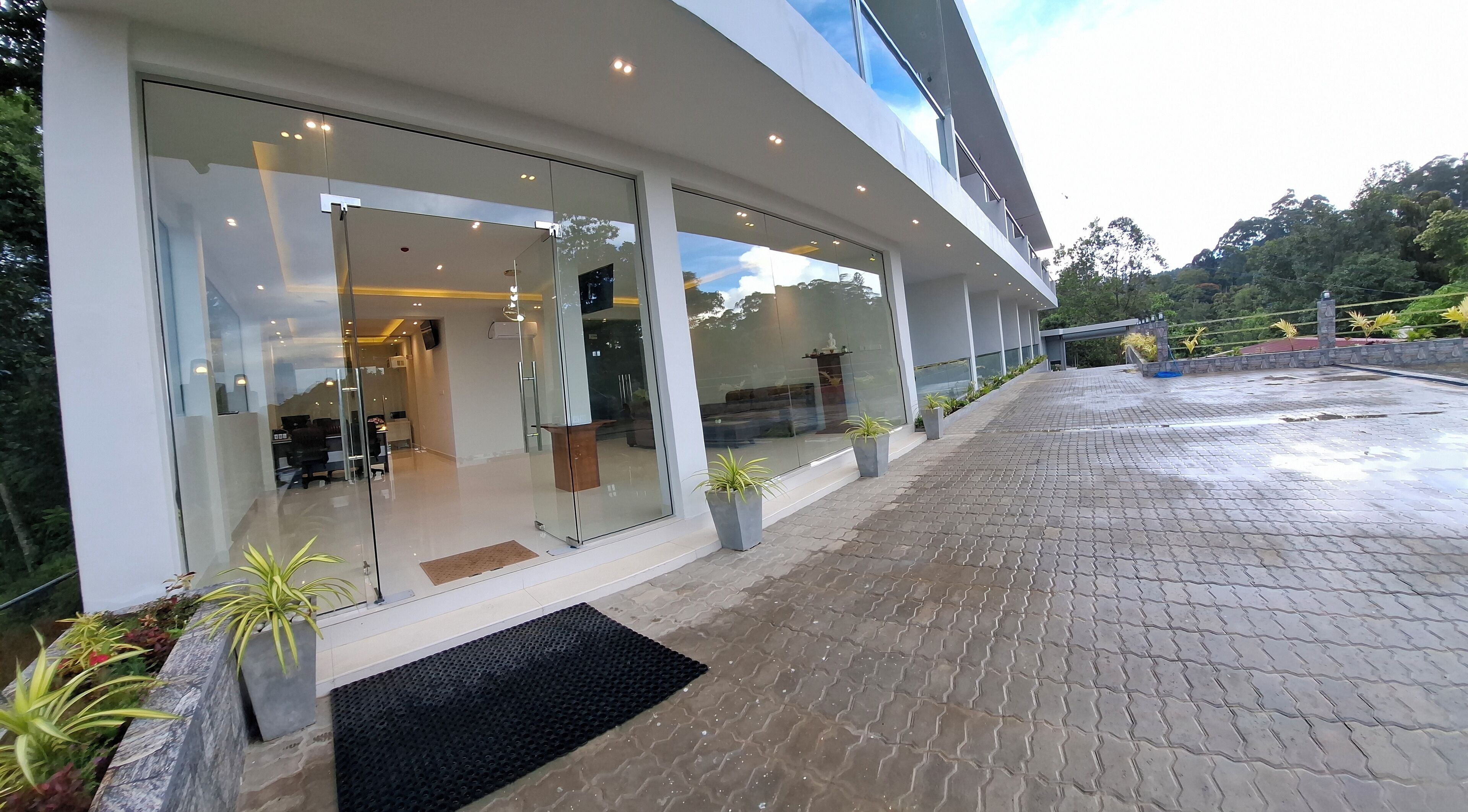 A modern building with large glass windows, a paved entrance area, and potted plants.