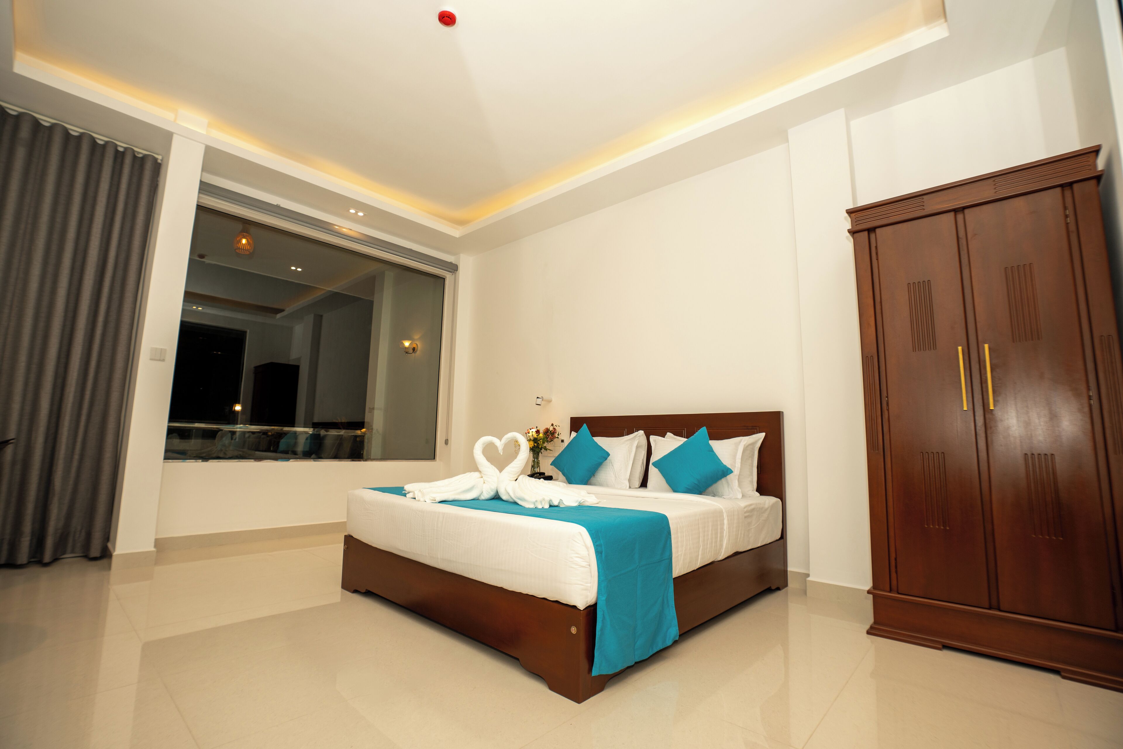 A hotel room with a large bed, a wardrobe, and a window with curtains.