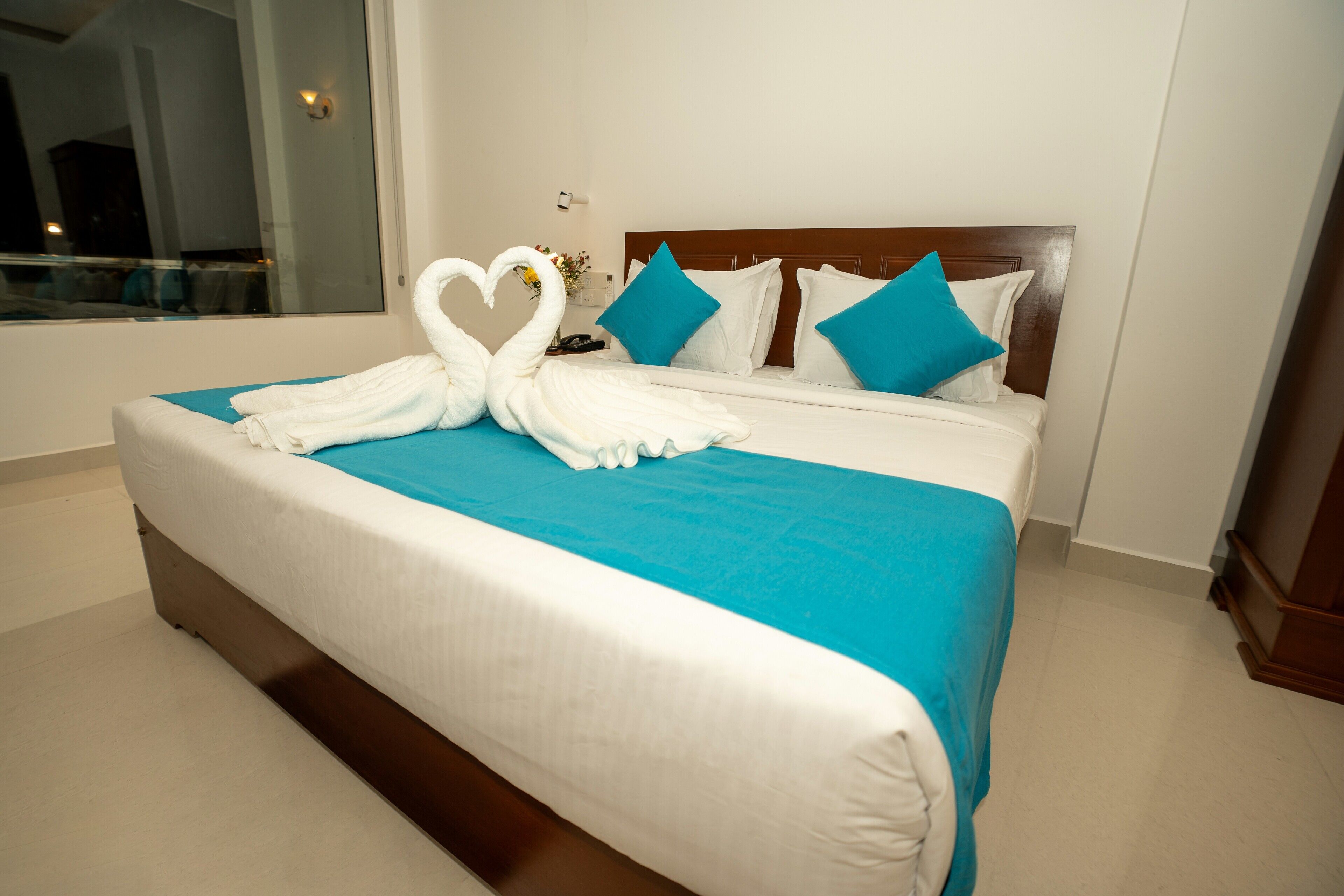 A hotel room with a large bed, a wooden headboard, and a view of the city through a large window.