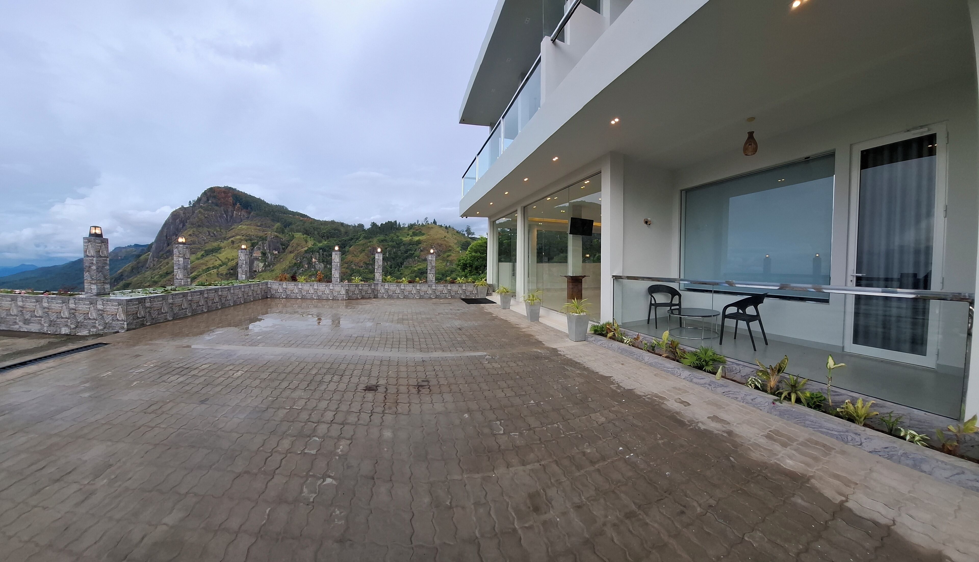 Un bâtiment moderne doté d’une terrasse dallée, d’un espace extérieur aménagé pour s’asseoir et offrant une vue sur un paysage montagneux.