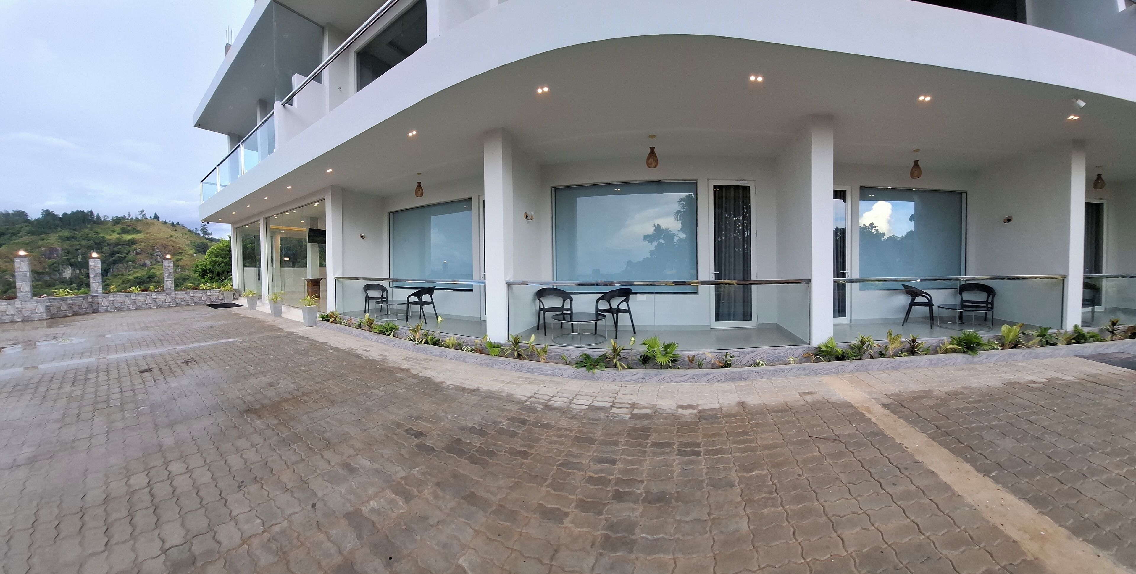 A modern building with a covered outdoor area featuring glass walls and black chairs.