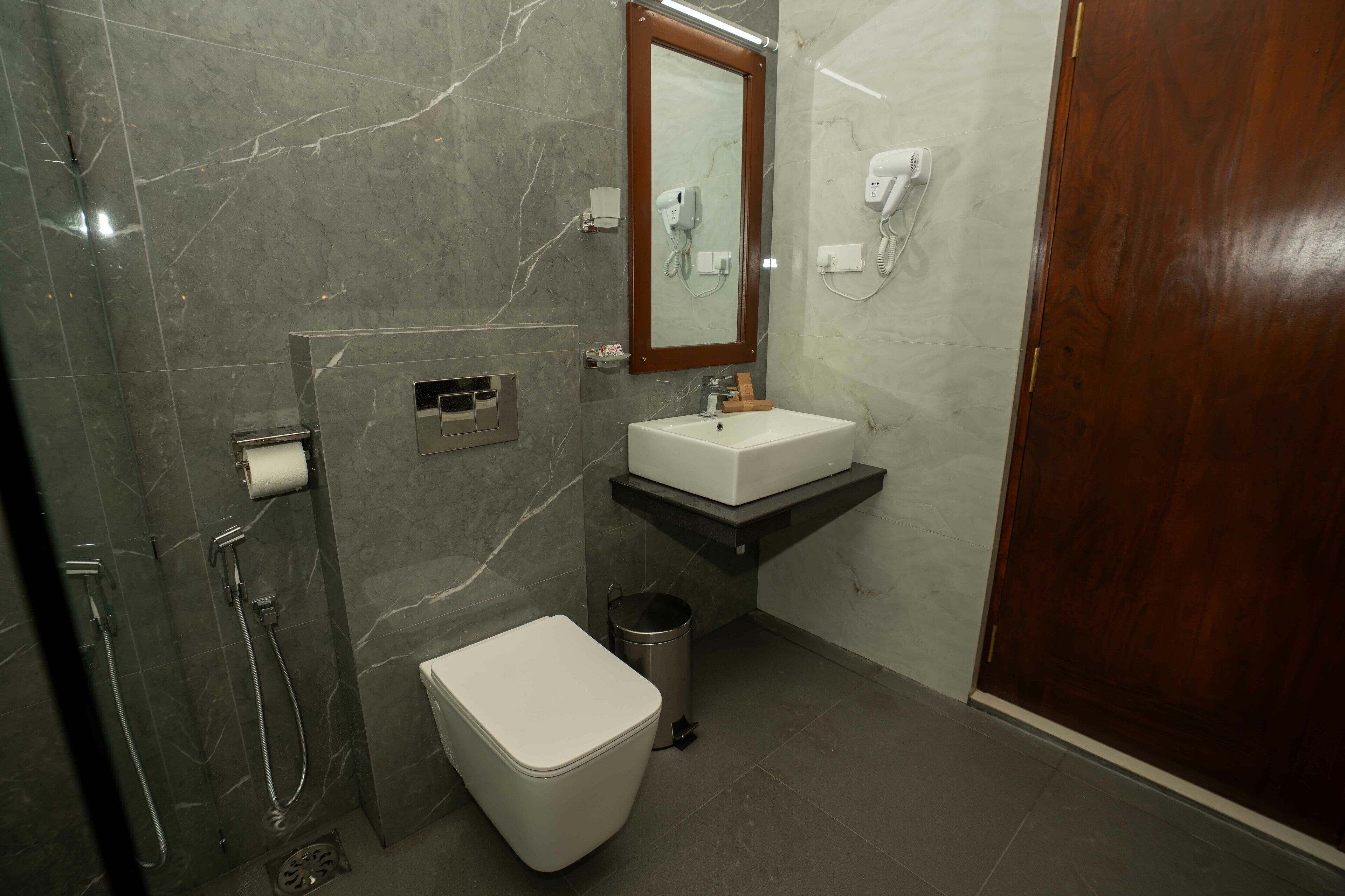 A modern bathroom with a marble wall, a white toilet, a sink with a wooden countertop, a mirror, and a shower area.