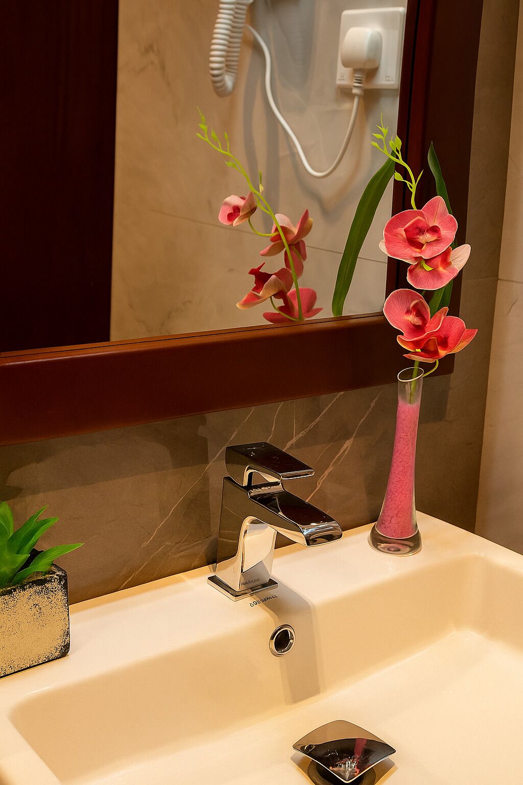 Un lavabo de salle de bain avec un robinet moderne, un vase contenant des orchidées roses et le reflet de la décoration de la salle de bain dans le miroir.