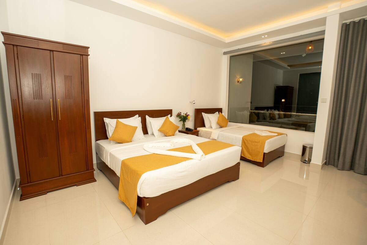 Habitación de hotel con dos camas, un armario, una mesita de noche y un ventanal grande.