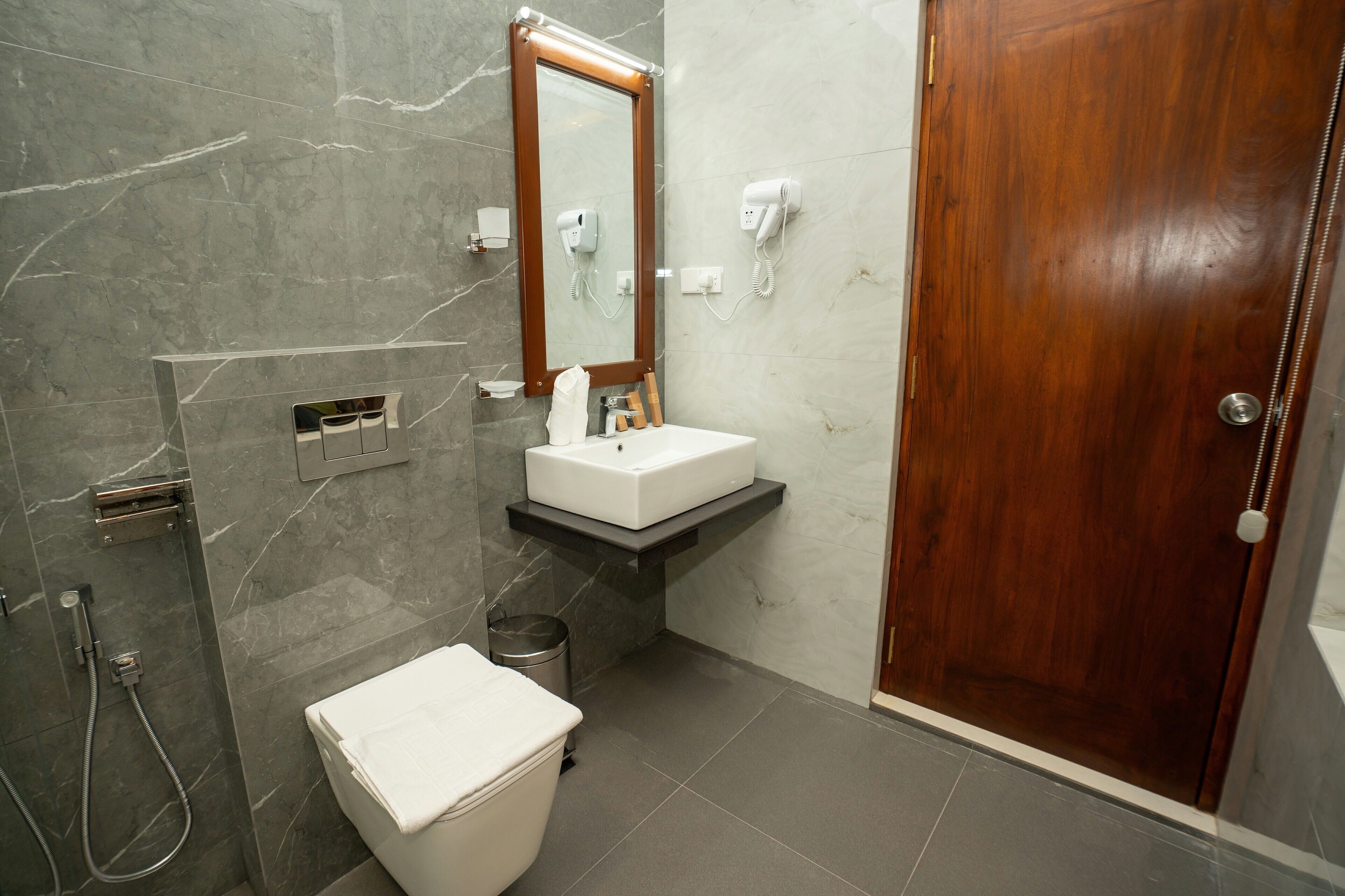 A bathroom with a marble wall, a wooden door, a white sink, a mirror, and a shower area.