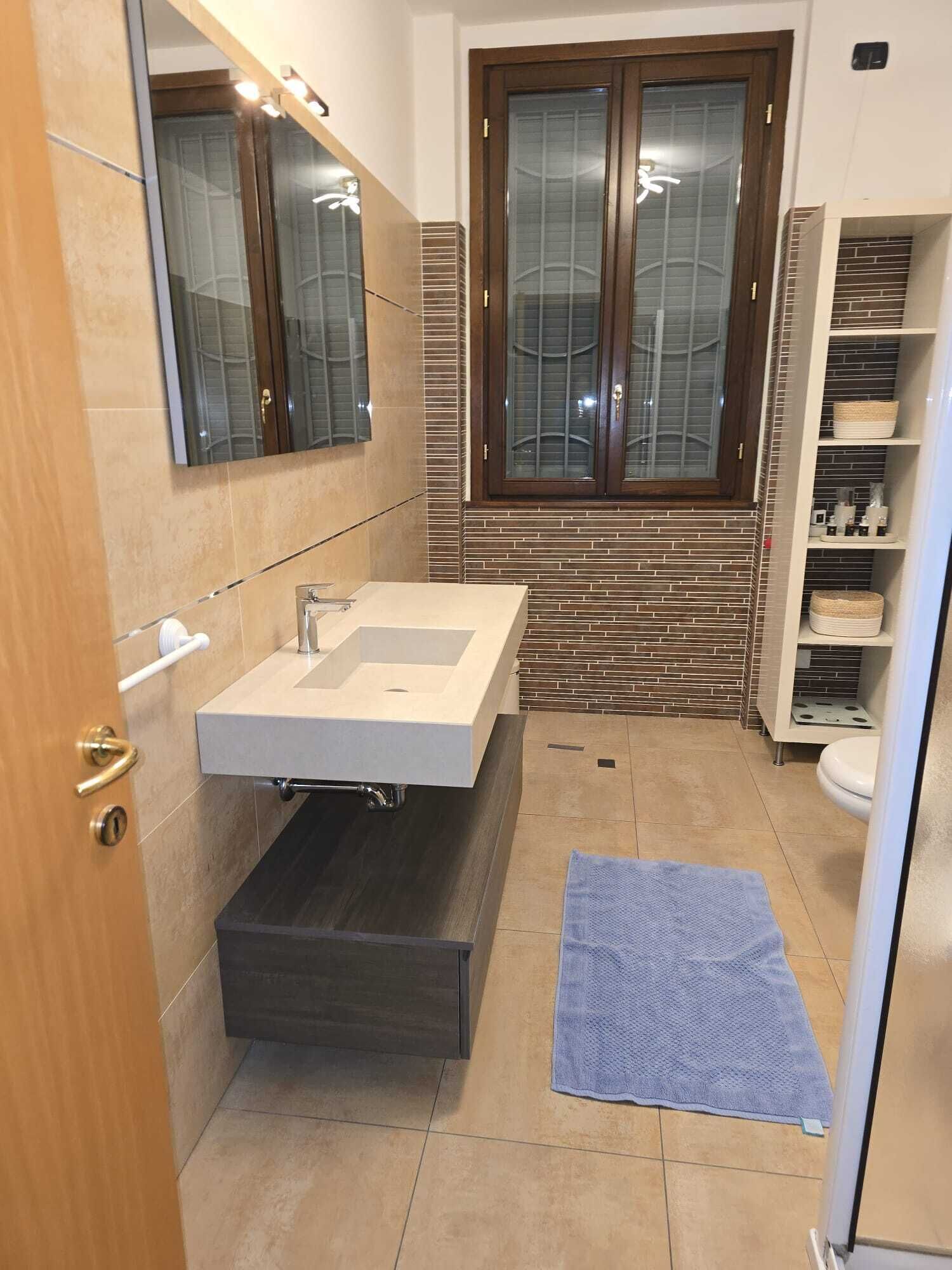 Une salle de bain moderne avec un grand miroir, un lavabo encastré, un porte-serviettes et une fenêtre donnant sur un beau paysage.