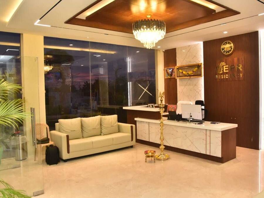 A modern reception area with a sofa, desk, chandelier, and large windows.