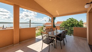 A balcony with a table and chairs, overlooking a body of water and buildings. - 3 bedroom lovely apartment in Maslenica (Maslenica)