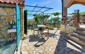 A stone patio with a table and chairs, a pergola, and a view of greenery and buildings in the background. - 3 bedroom awesome apartment in Maslenica (Maslenica)