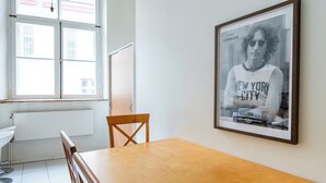 Une pièce avec une table à manger en bois, une affiche encadrée au mur et une fenêtre donnant sur des immeubles.