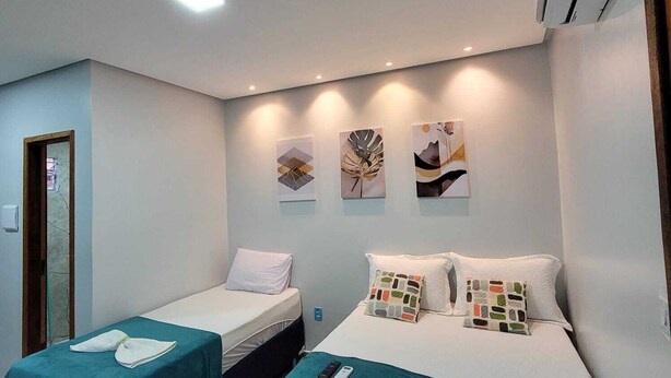 Habitación de hotel con dos camas, cada una con una colcha color turquesa y almohadas blancas. Hay tres obras de arte colgadas en la pared sobre las camas.