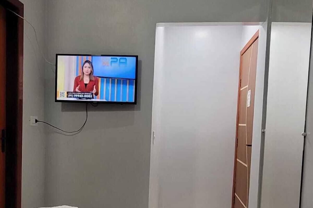 Ett hotellrum med en säng, en tv som är monterad på väggen och en dörr som leder till ett annat rum.