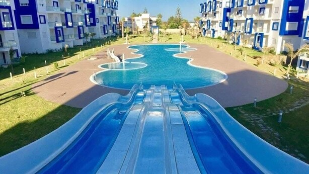 A water slide leading to a pool surrounded by modern buildings with balconies. - Apparently delux in a complex with three pools (Cabo Negro)