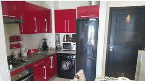 A compact kitchen with red cabinets, a microwave, a washing machine, and a refrigerator. - Apparently delux in a complex with three pools (Cabo Negro)